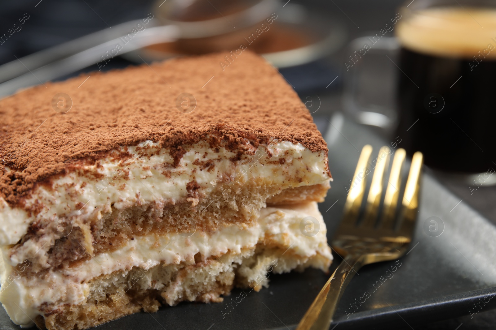 Photo of Piece of tasty tiramisu and fork on black table, closeup