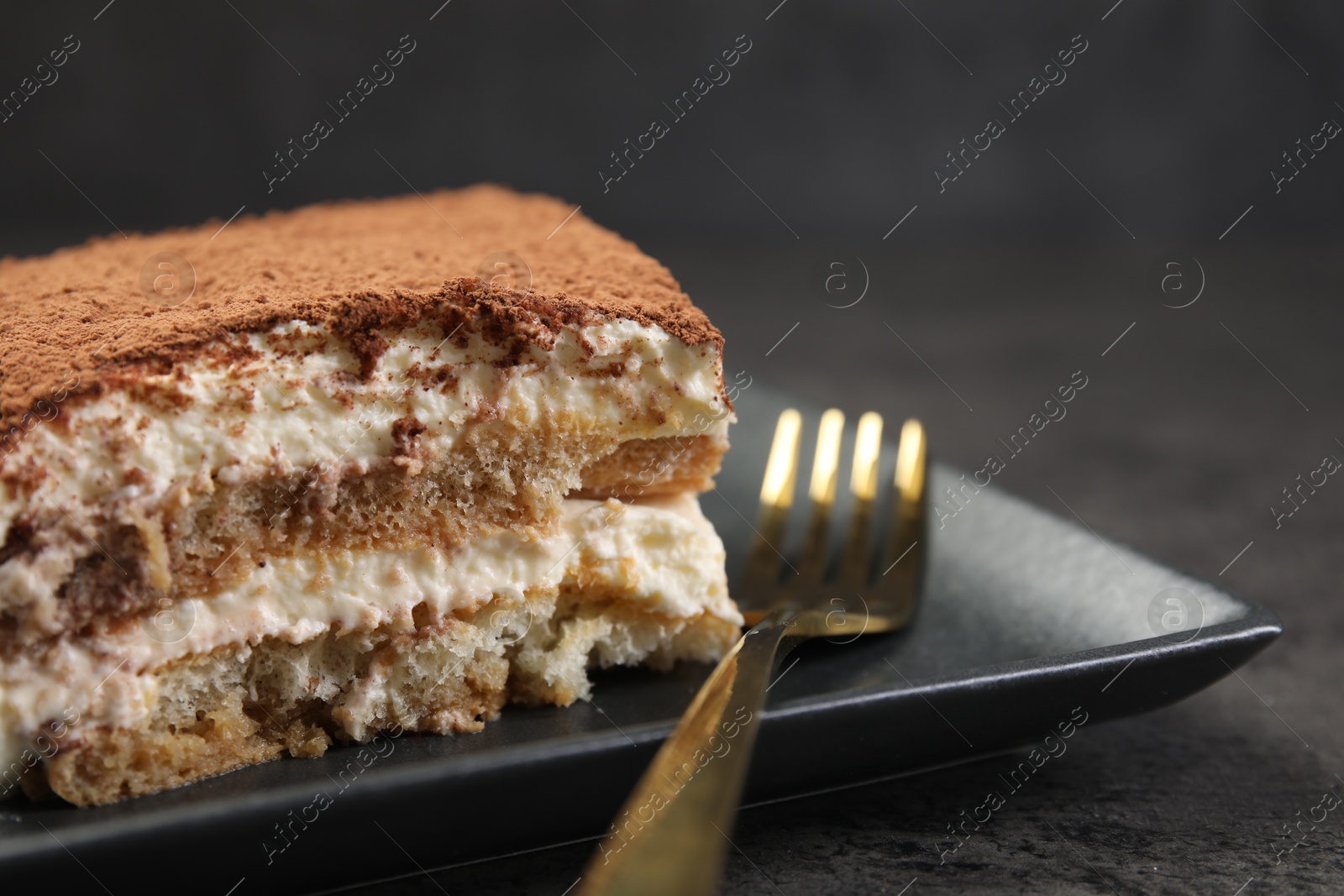 Photo of Piece of tasty tiramisu and fork on black table, closeup