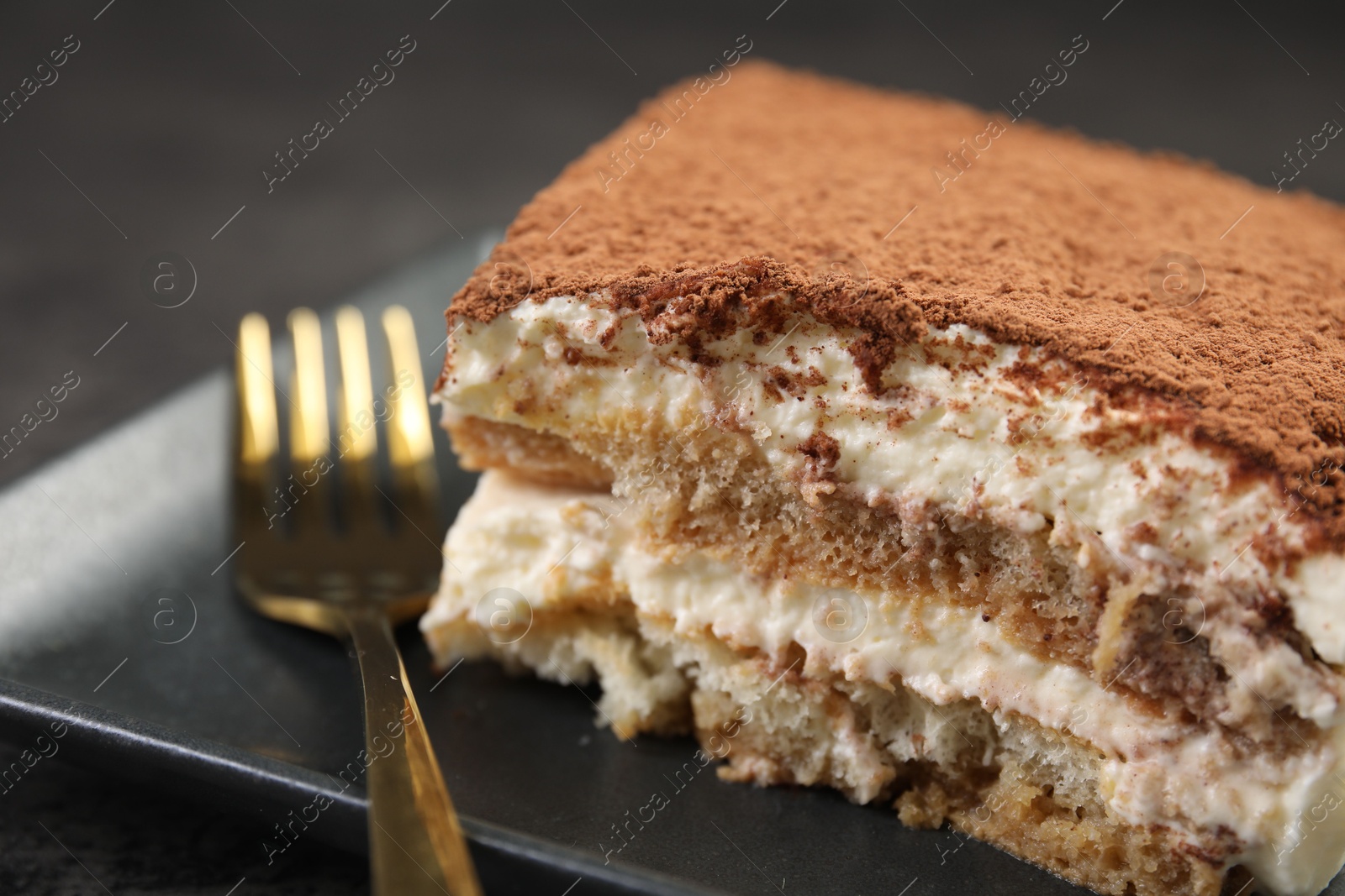 Photo of Piece of tasty tiramisu and fork on black table, closeup