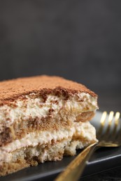 Photo of Piece of tasty tiramisu and fork on black table, closeup