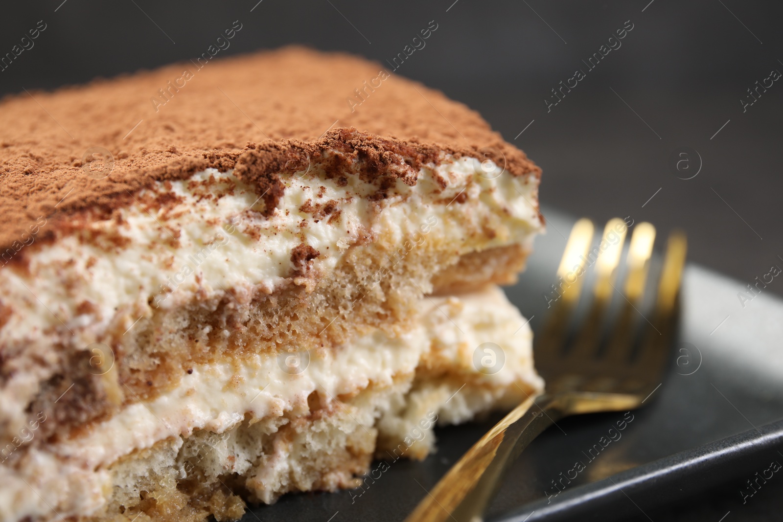 Photo of Piece of tasty tiramisu and fork on black table, closeup