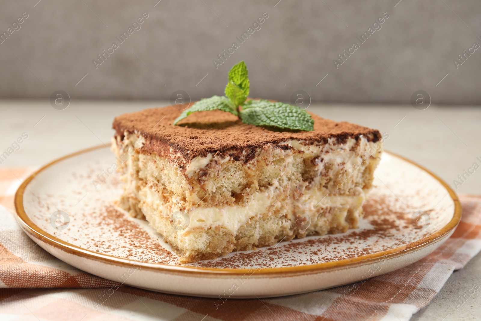 Photo of Piece of tasty tiramisu with fresh mint on beige table, closeup