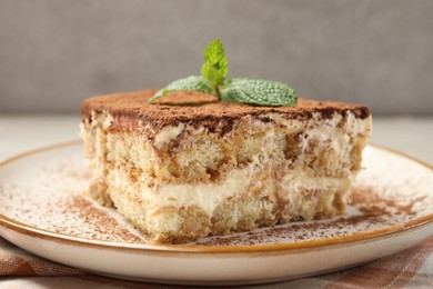 Photo of Piece of tasty tiramisu with fresh mint on beige table, closeup