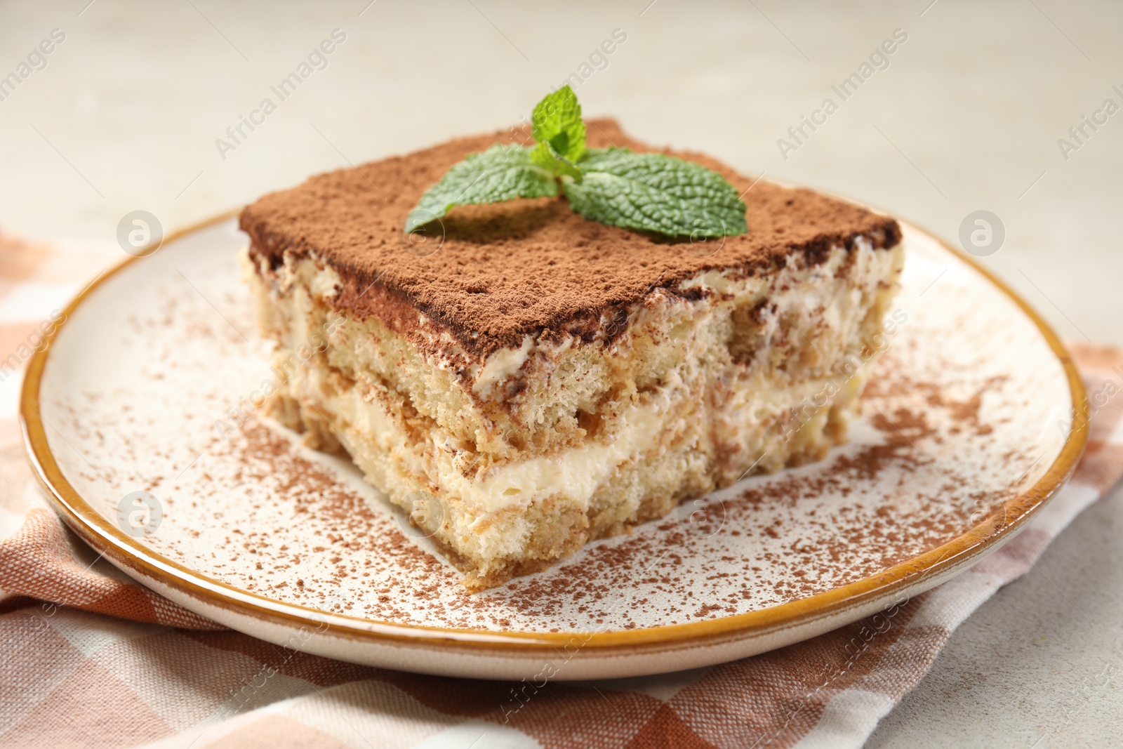 Photo of Piece of tasty tiramisu with fresh mint on beige table, closeup