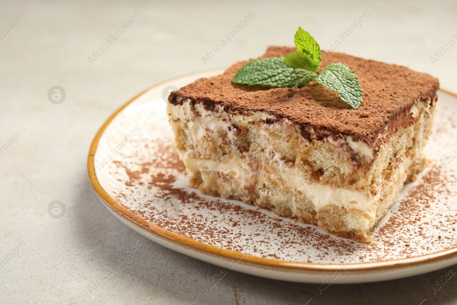 Photo of Piece of tasty tiramisu with fresh mint on beige table, closeup