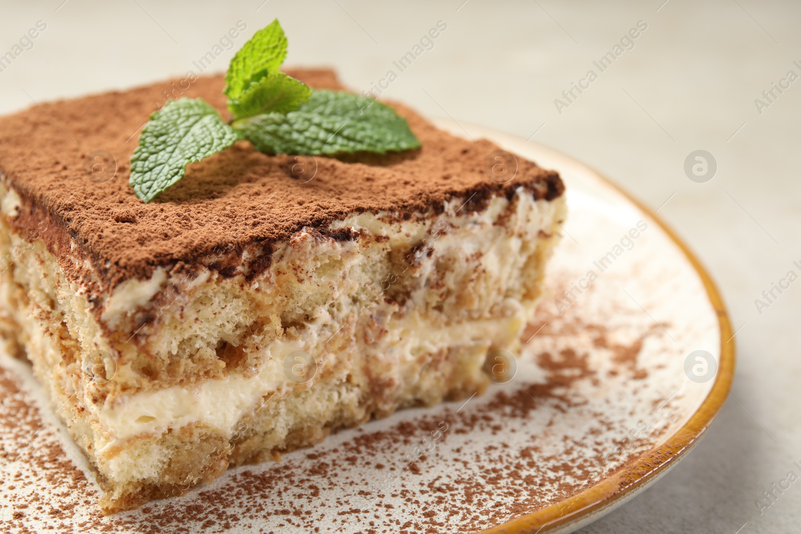 Photo of Piece of tasty tiramisu with fresh mint on beige table, closeup