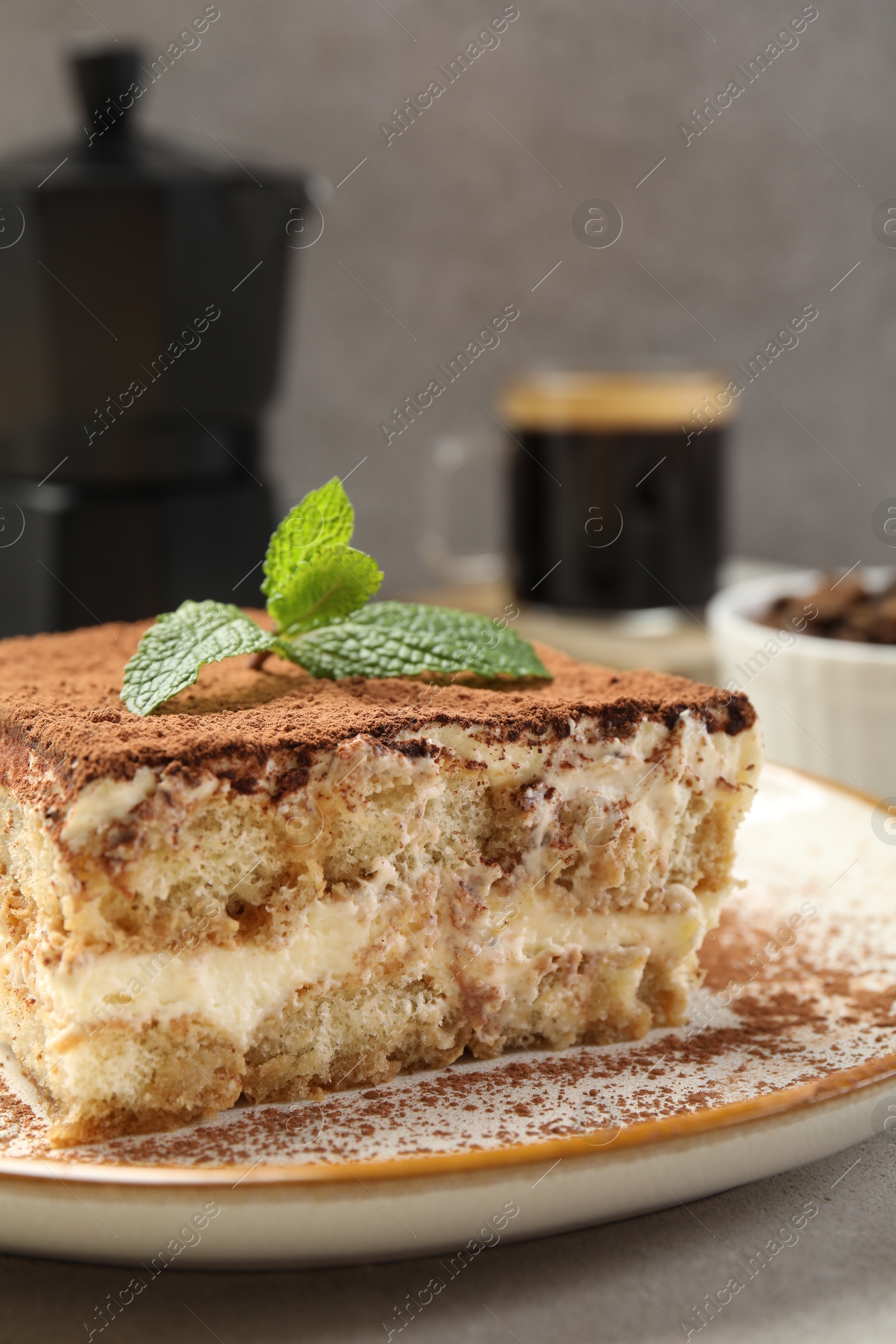 Photo of Piece of tasty tiramisu with fresh mint on beige table, closeup