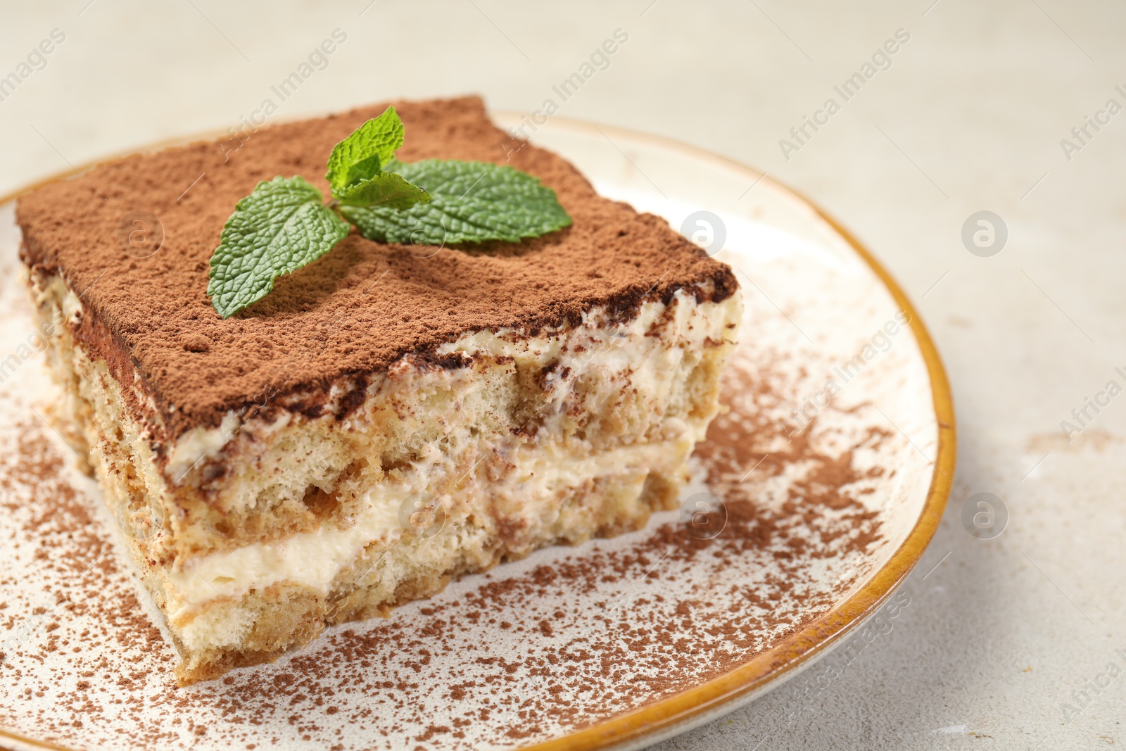 Photo of Piece of tasty tiramisu with fresh mint on beige table, closeup