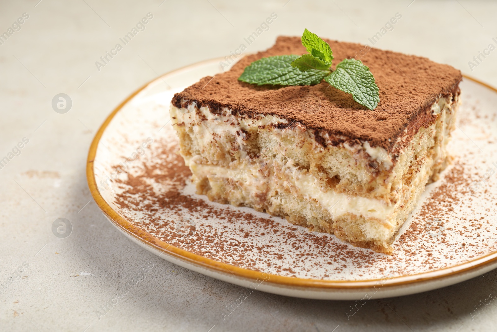 Photo of Piece of tasty tiramisu with fresh mint on beige table, closeup