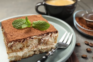 Photo of Piece of tasty tiramisu with fresh mint on grey table, closeup