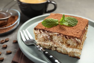 Photo of Piece of tasty tiramisu with fresh mint on grey table, closeup