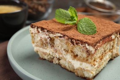 Photo of Piece of tasty tiramisu with fresh mint on table, closeup