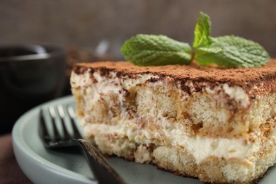 Photo of Piece of tasty tiramisu with fresh mint on table, closeup