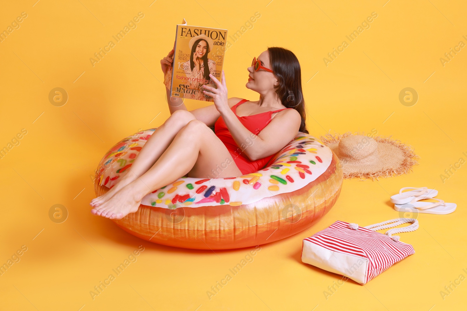 Photo of Beautiful woman with beach accessories reading magazine on yellow background