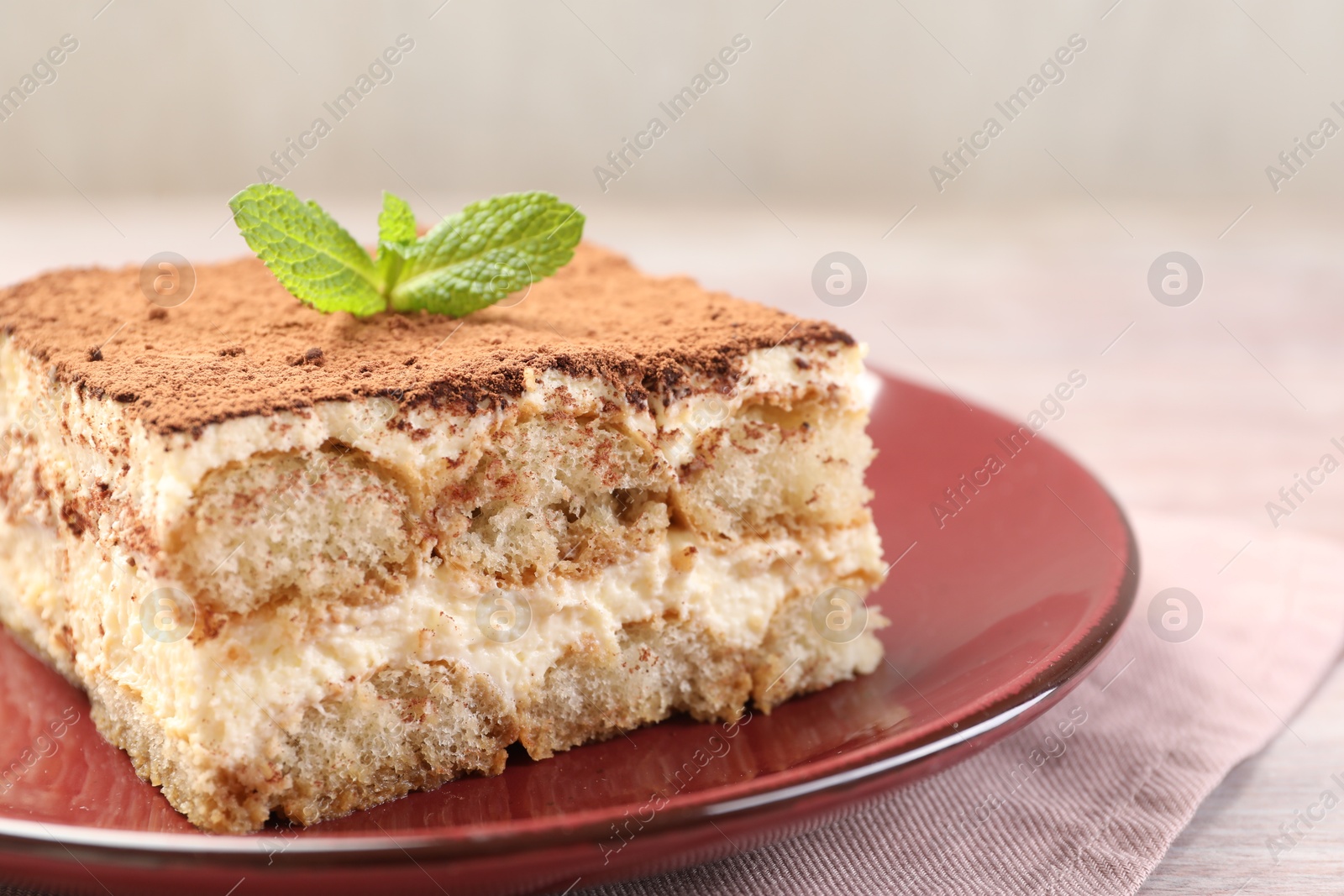 Photo of Delicious tiramisu with mint on light wooden table, closeup