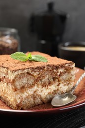 Photo of Delicious tiramisu with mint on black wooden board, closeup