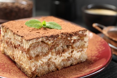 Photo of Delicious tiramisu with mint on black wooden board, closeup