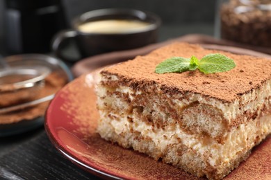 Photo of Delicious tiramisu with mint on black wooden board, closeup