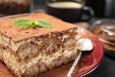 Photo of Delicious tiramisu with mint on black wooden board, closeup