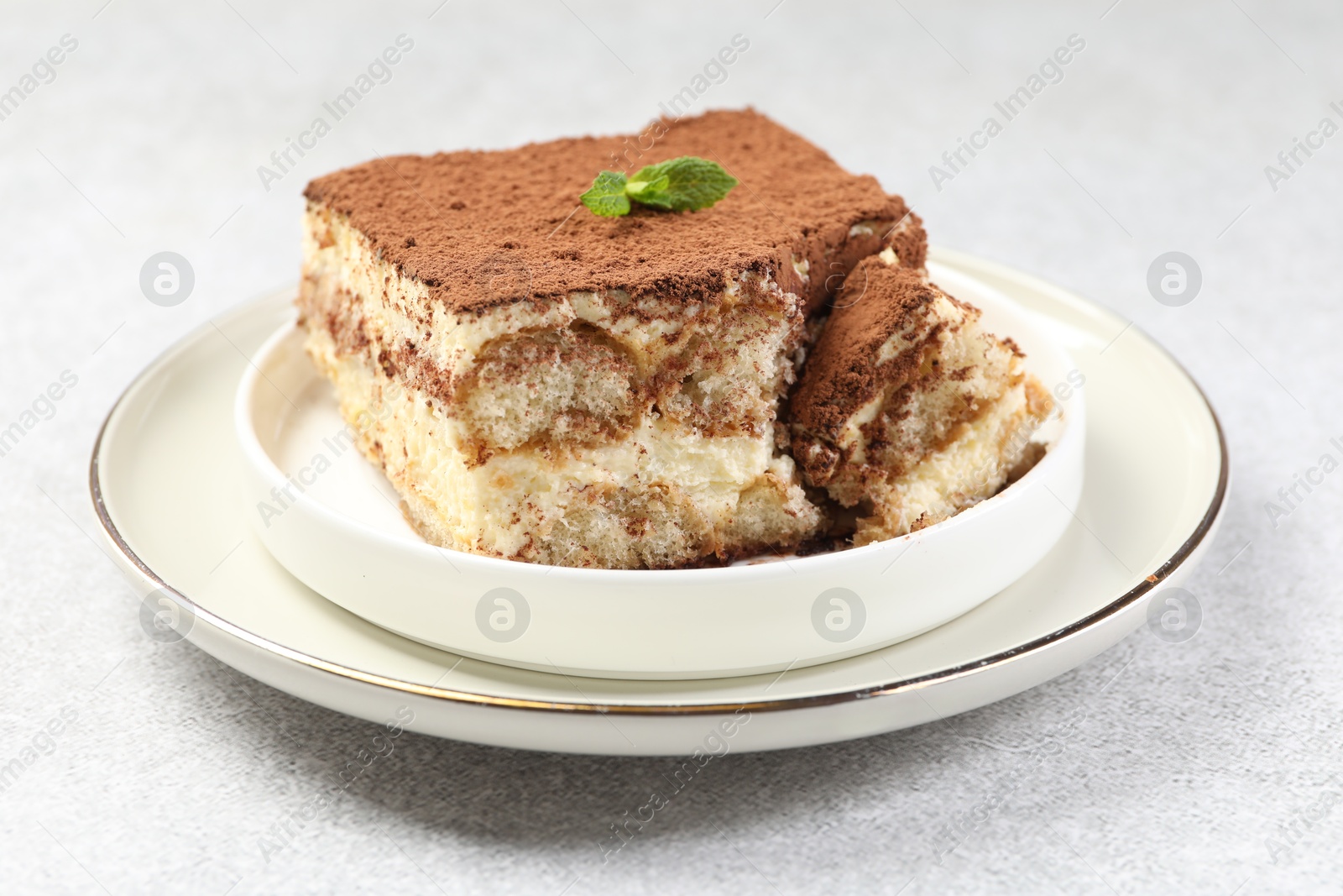 Photo of Delicious tiramisu with mint on light table, closeup