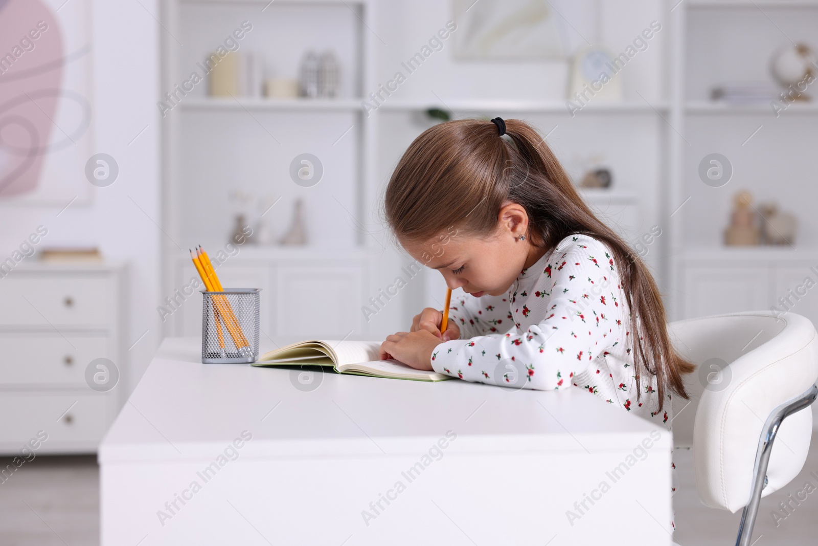 Photo of Girl with incorrect posture doing homework at white desk indoors