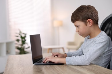 Photo of Boy with incorrect posture using laptop at wooden desk indoors