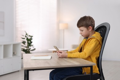 Photo of Boy with correct posture using smartphone at wooden desk indoors