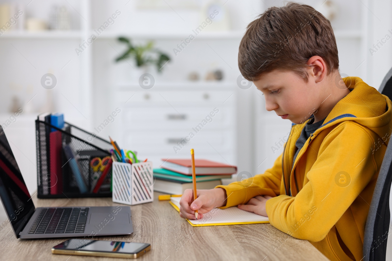 Photo of Boy with correct posture doing homework at wooden desk indoors