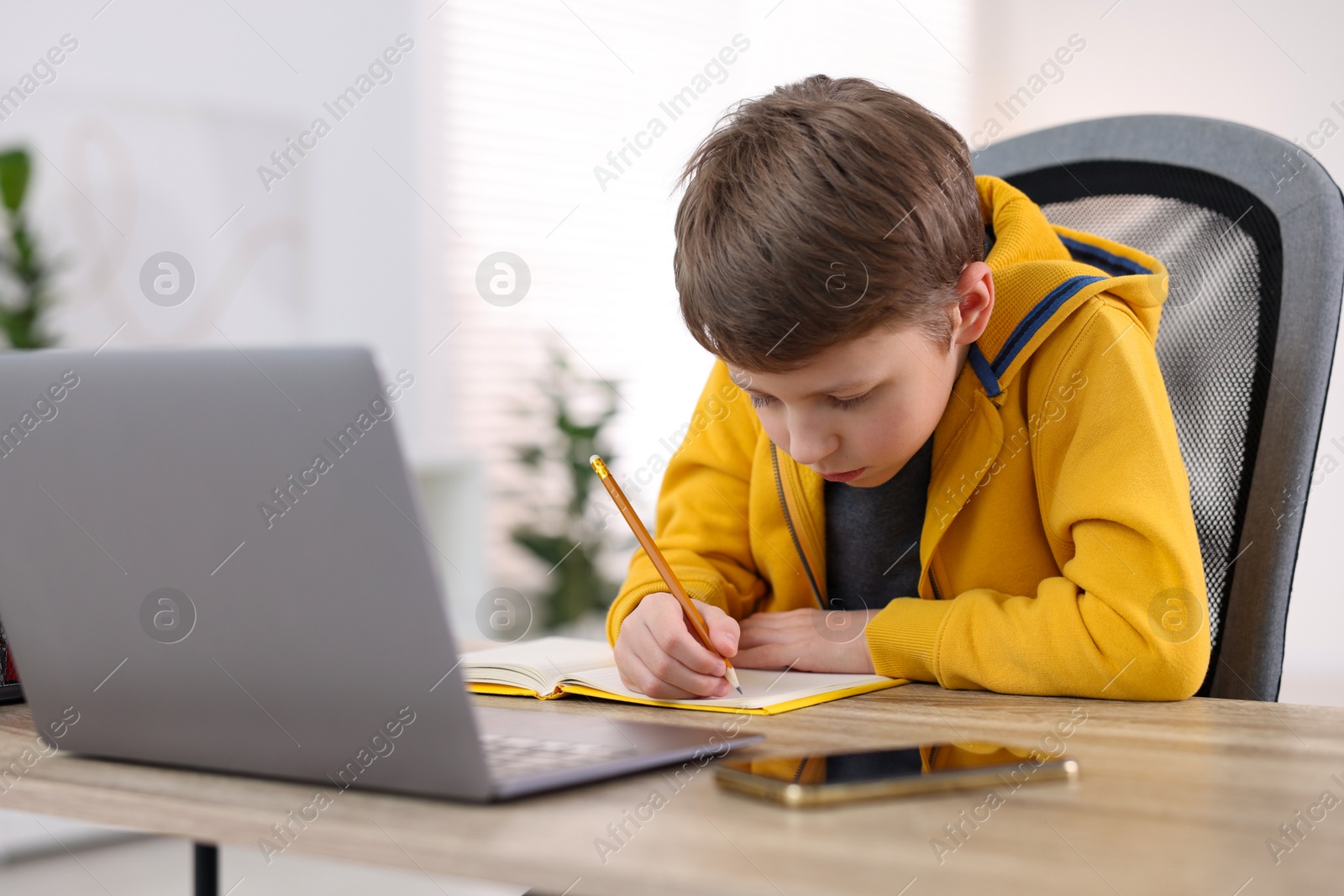 Photo of Boy with incorrect posture using laptop at wooden desk indoors