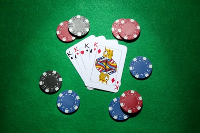 Photo of Poker chips and playing cards on green table, flat lay