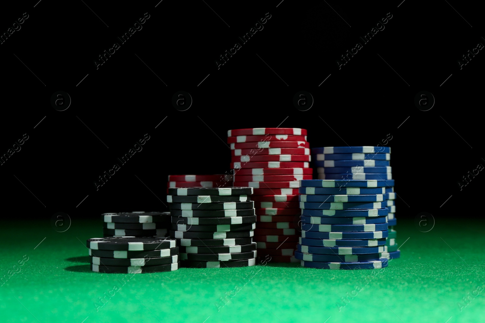 Photo of Stacks of poker chips on green table against dark background, closeup