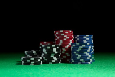 Stacks of poker chips on green table against dark background, closeup