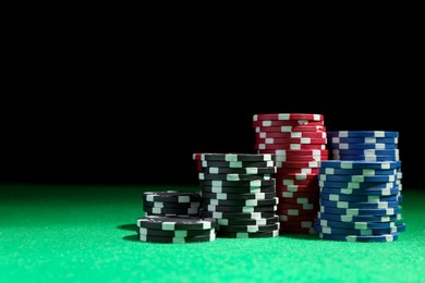 Stacks of poker chips on green table against dark background, space for text