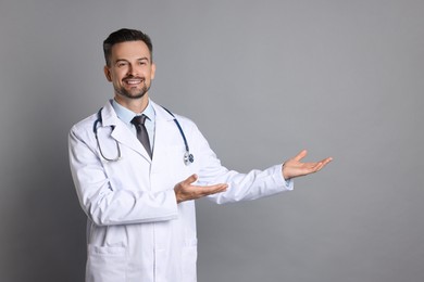 Photo of Smiling doctor with stethoscope pointing at something on grey background