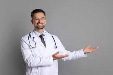 Photo of Smiling doctor with stethoscope pointing at something on grey background