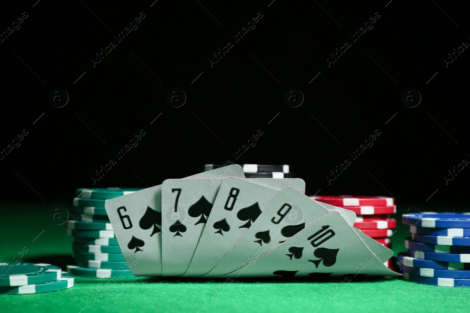 Photo of Playing cards and poker chips on green table against dark background