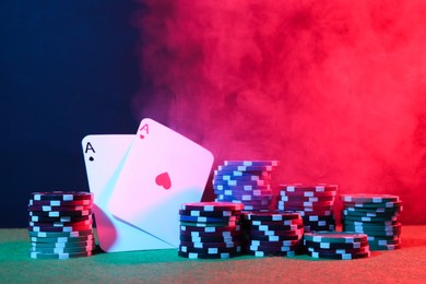 Photo of Poker chips and playing cards on green table in neon lights