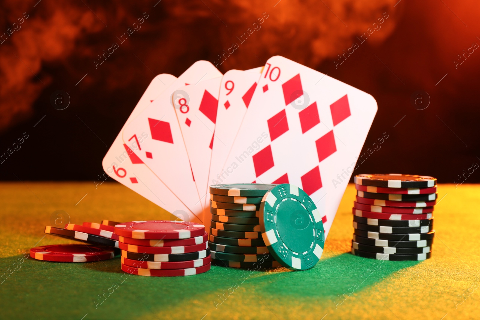 Photo of Poker chips and playing cards on green table in neon lights