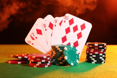 Poker chips and playing cards on green table in neon lights