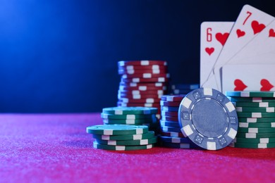 Photo of Poker chips and playing cards on pink table in neon lights, closeup. Space for text