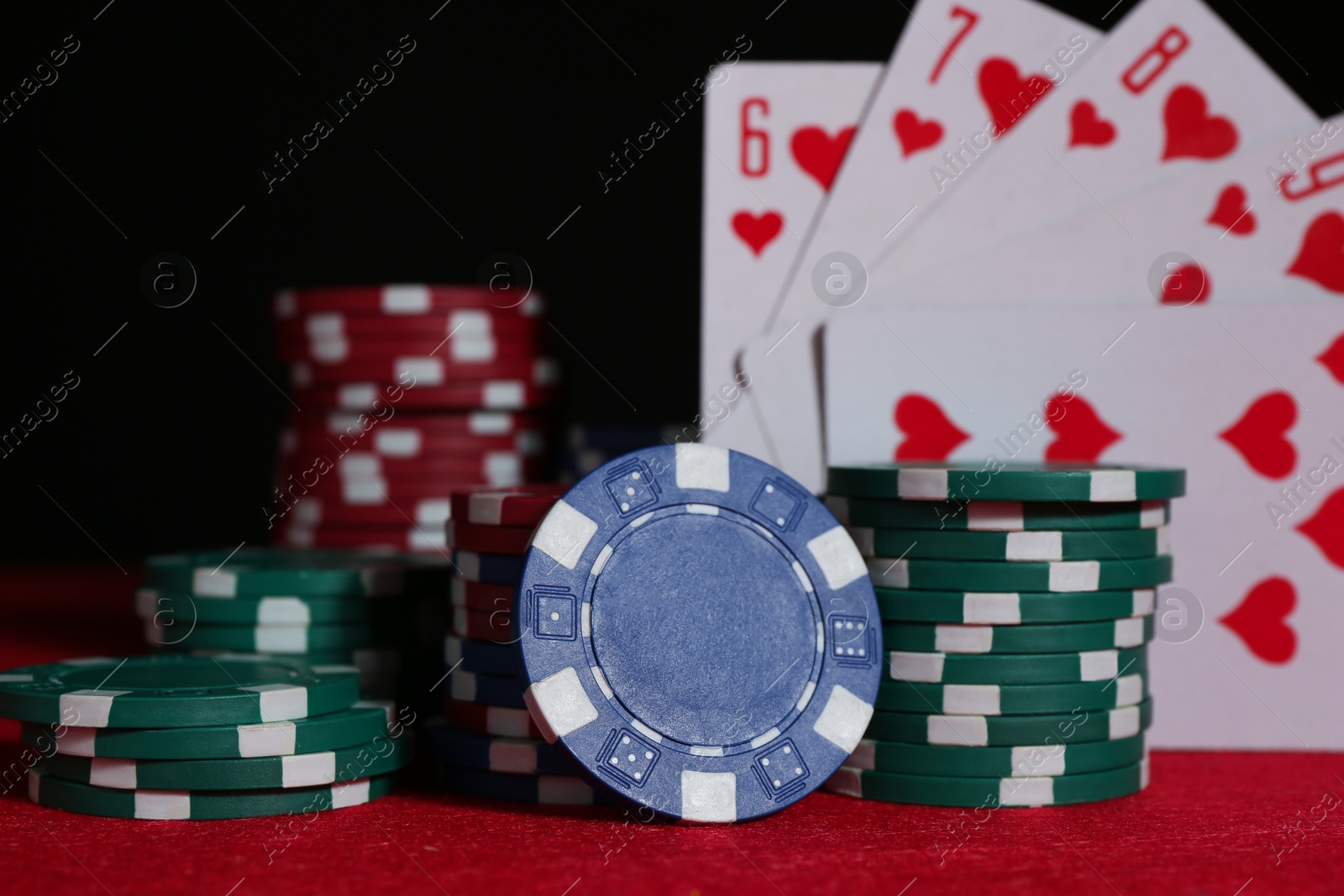 Photo of Poker chips and playing cards on red table, closeup