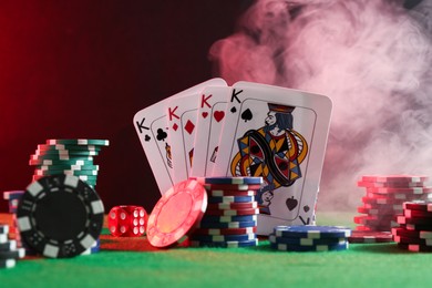 Photo of Poker chips, dice and playing cards on green table in neon lights, closeup