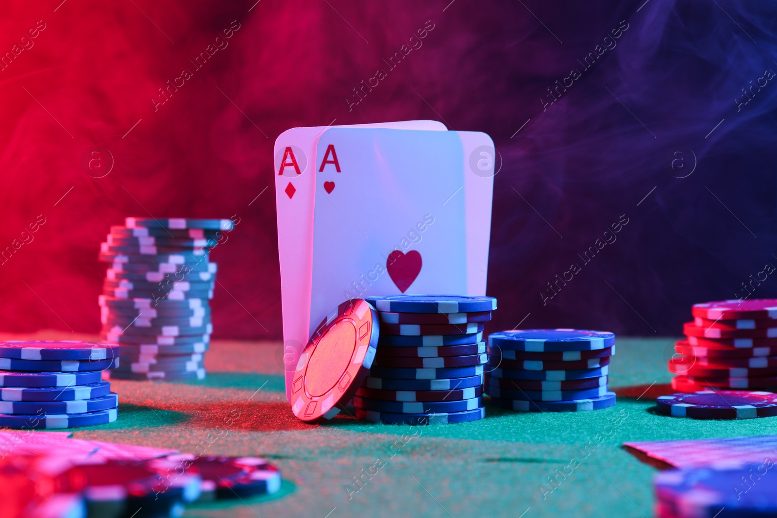 Photo of Poker chips and playing cards on green table in neon lights, closeup