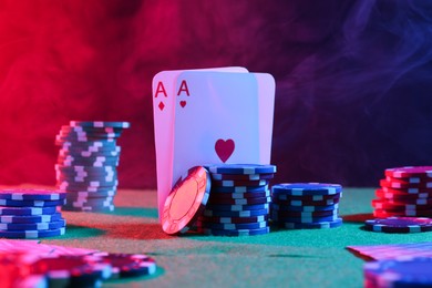 Poker chips and playing cards on green table in neon lights, closeup