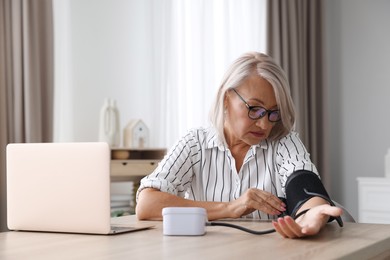 Photo of Woman measuring blood pressure at wooden table indoors