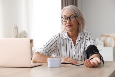 Photo of Woman measuring blood pressure at wooden table indoors