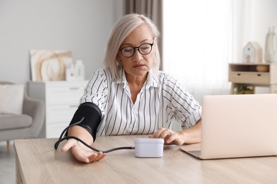 Photo of Woman measuring blood pressure at wooden table indoors