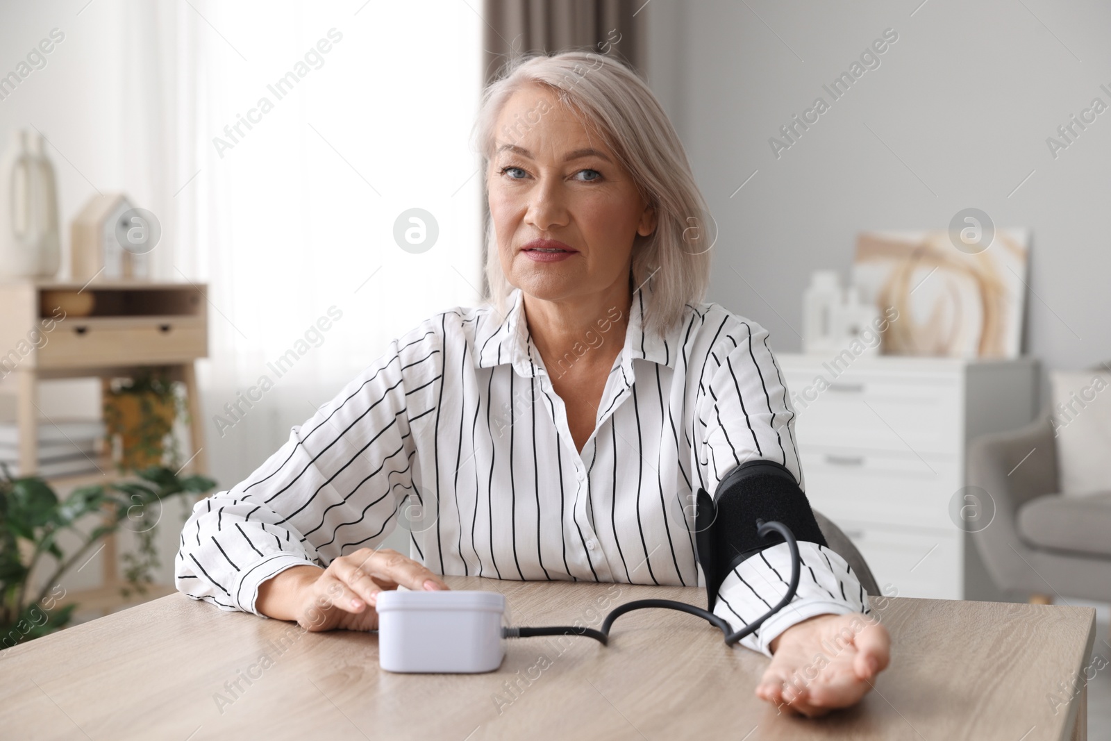 Photo of Woman measuring blood pressure at wooden table indoors