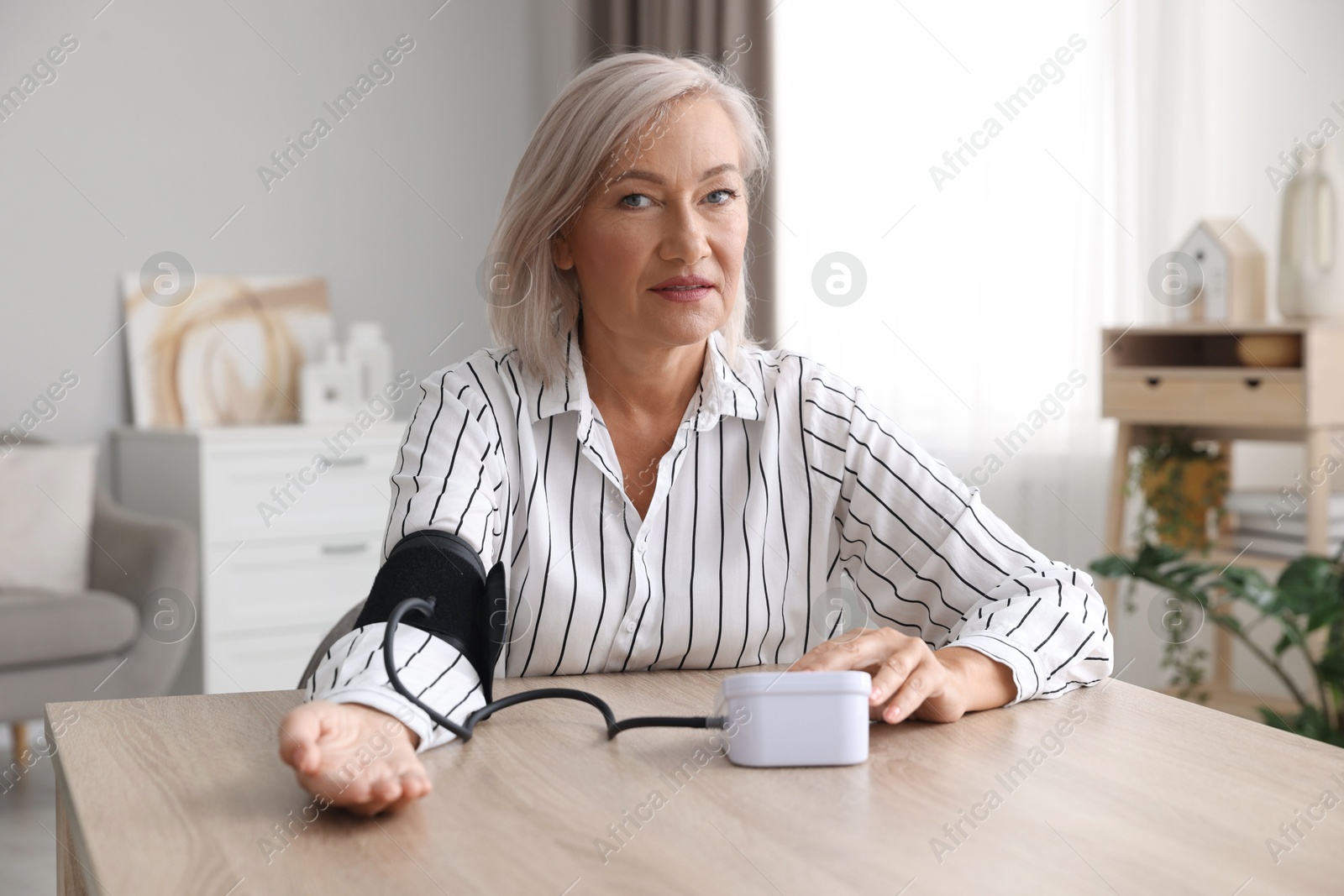 Photo of Woman measuring blood pressure at wooden table indoors