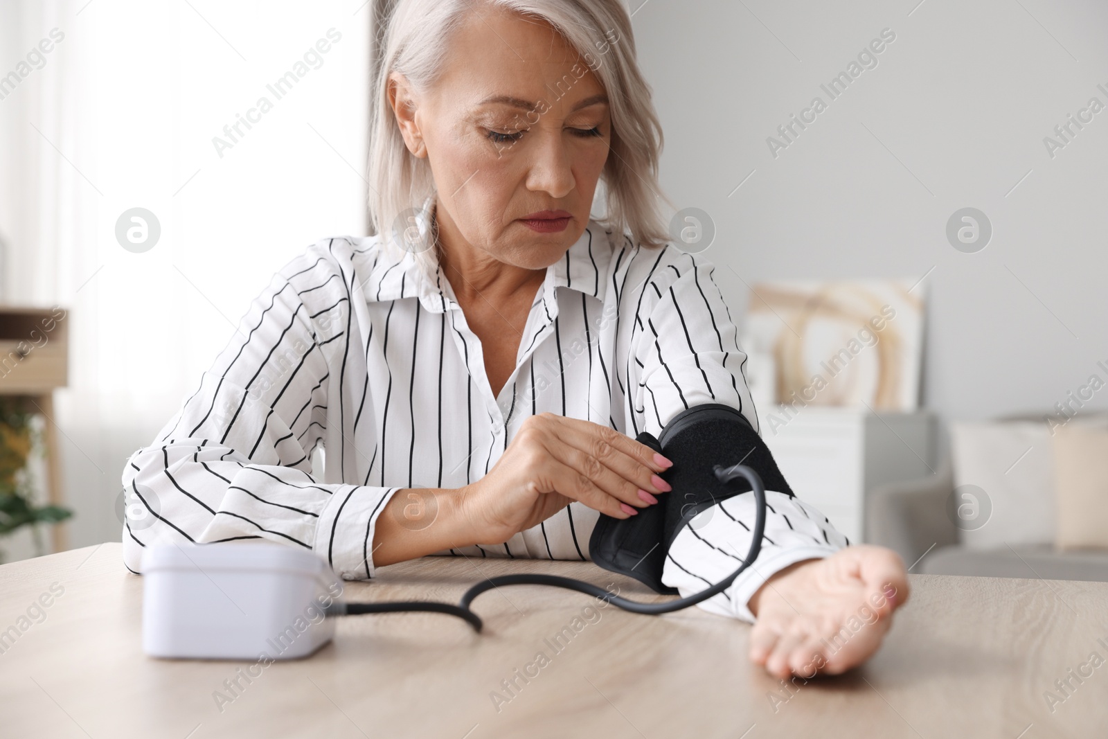 Photo of Woman measuring blood pressure at wooden table indoors